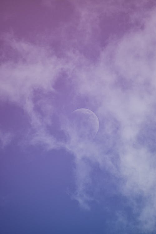 From below of white moon and fluffy clouds floating on blue sky on sunny day