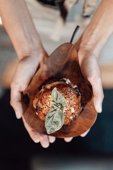 Close-up of hands holding a gourmet stuffed eggplant topped with basil, perfect for culinary presentations.