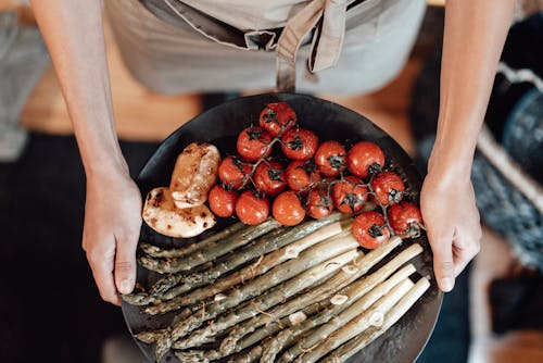 Person Holding Black Plate with Cherry Tomatoes and Asparagus