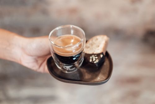 Free Hand holding espresso cup and chocolate on a wooden plate, blurred background. Stock Photo