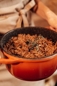 Close-up of a cooked orzo dish garnished with herbs in a rustic orange pot, creating a warm and homely feel.