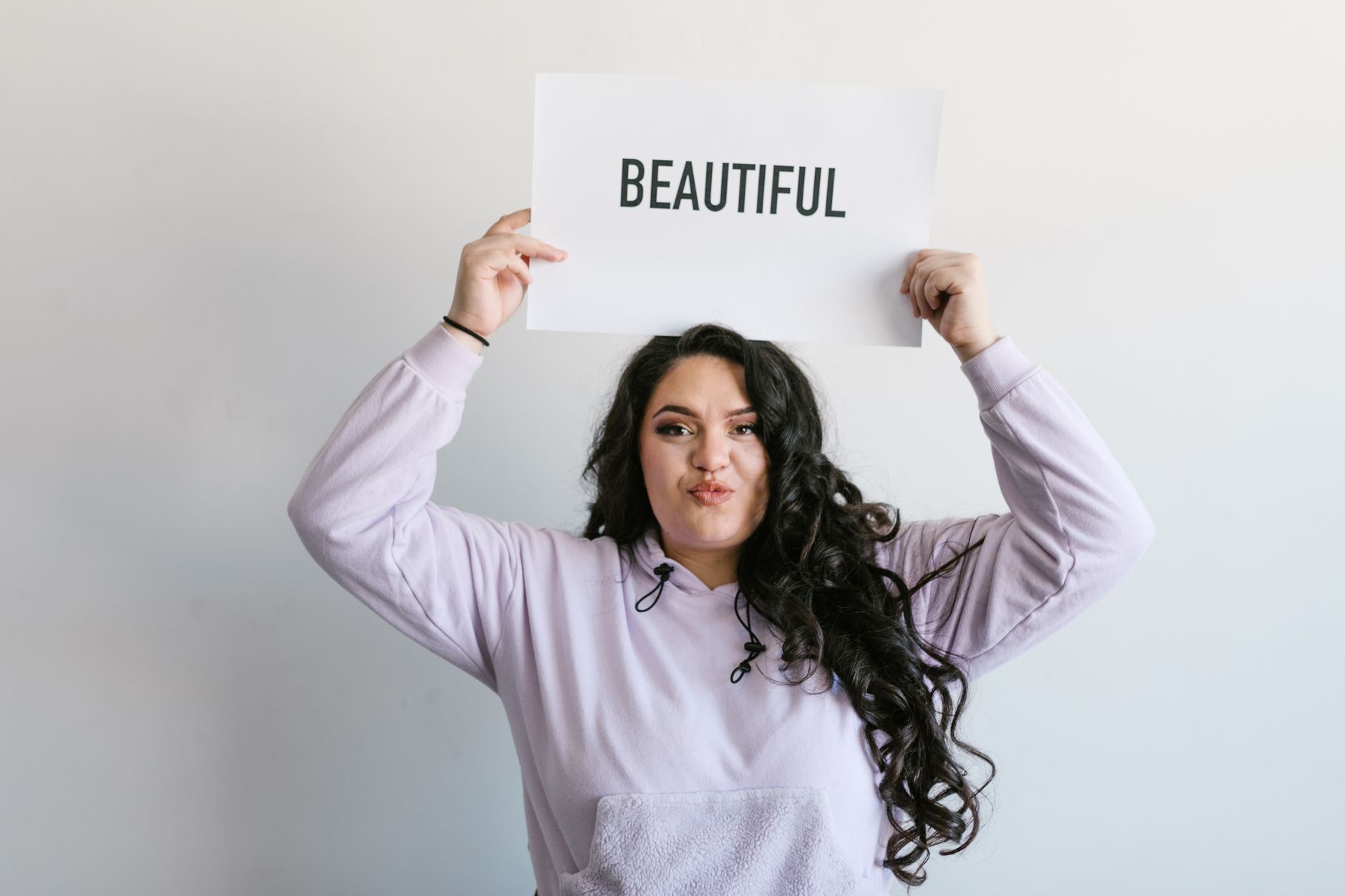 Plus size woman joyfully poses with a self-love sign, emphasizing beauty and confidence.