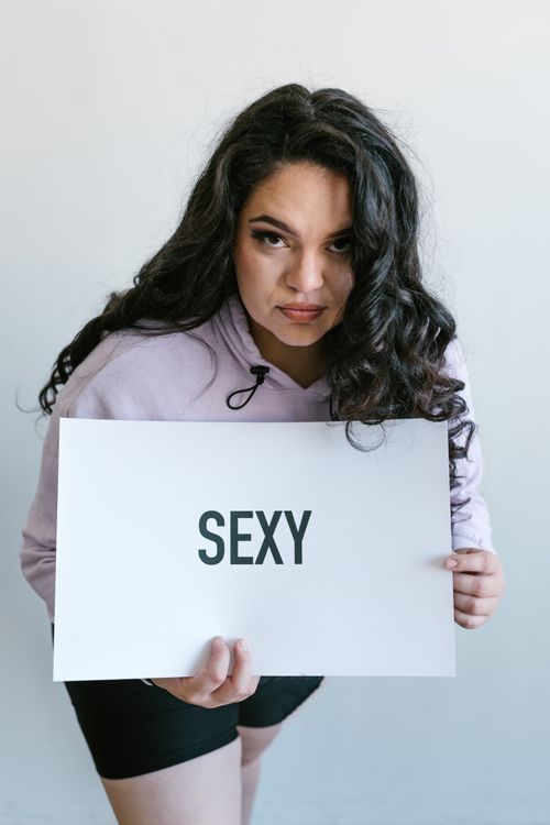 Free Young woman confidently holding a sign with 'sexy' written on it, indoors. Stock Photo