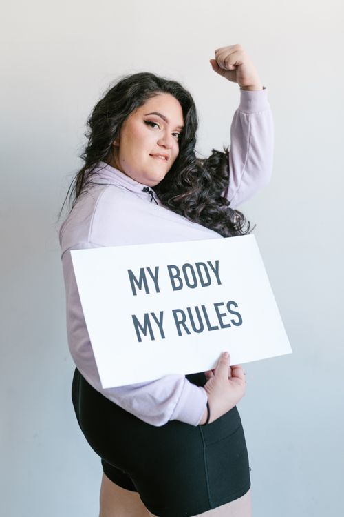 Free A confident plus-size woman poses with a 'My Body, My Rules' sign, promoting self-love and empowerment. Stock Photo