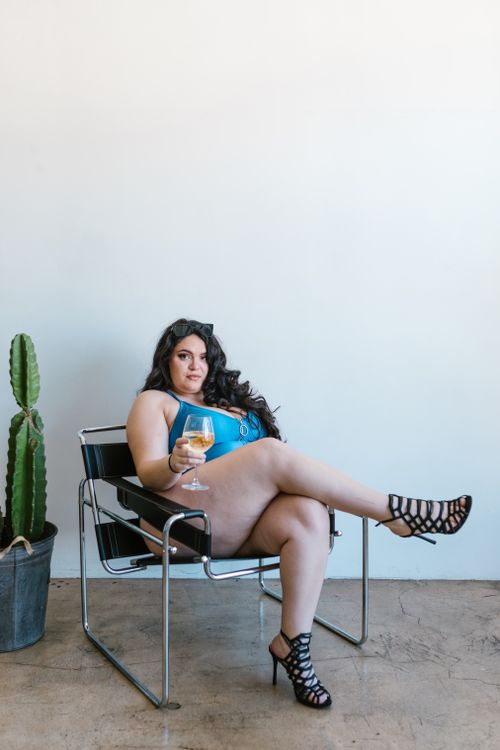 Free Plus-size woman in swimsuit sitting stylishly with wine indoors, embracing body positivity. Stock Photo