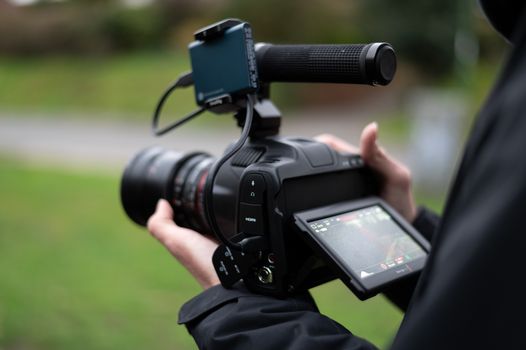 Cinematic DSLR camera being held outdoors, capturing video with blurred background.