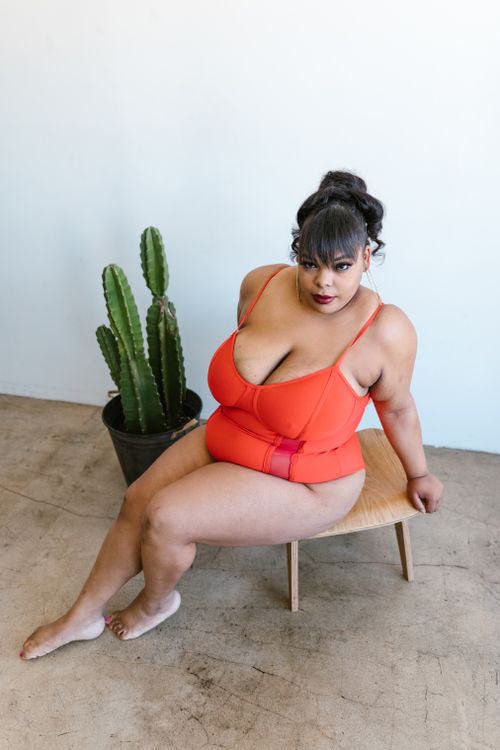 Free A plus-size woman sits confidently in a red swimsuit next to a cactus, embracing body positivity. Stock Photo