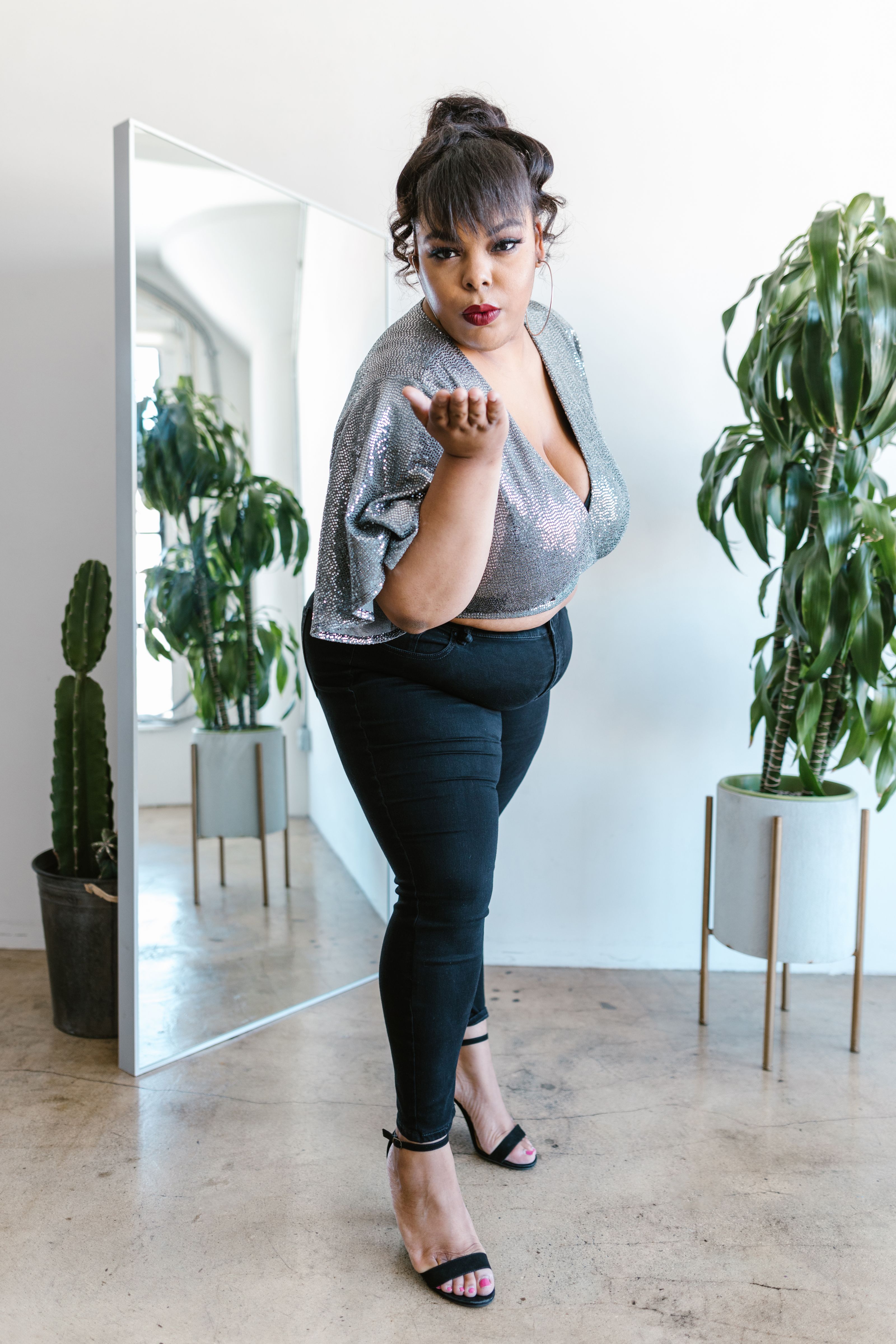 Mulher plus size posando com confiança em um traje estiloso com espelho e plantas internas.