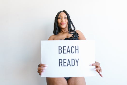 A confident woman in swimwear holding a 'BEACH READY' sign, embracing body positivity.