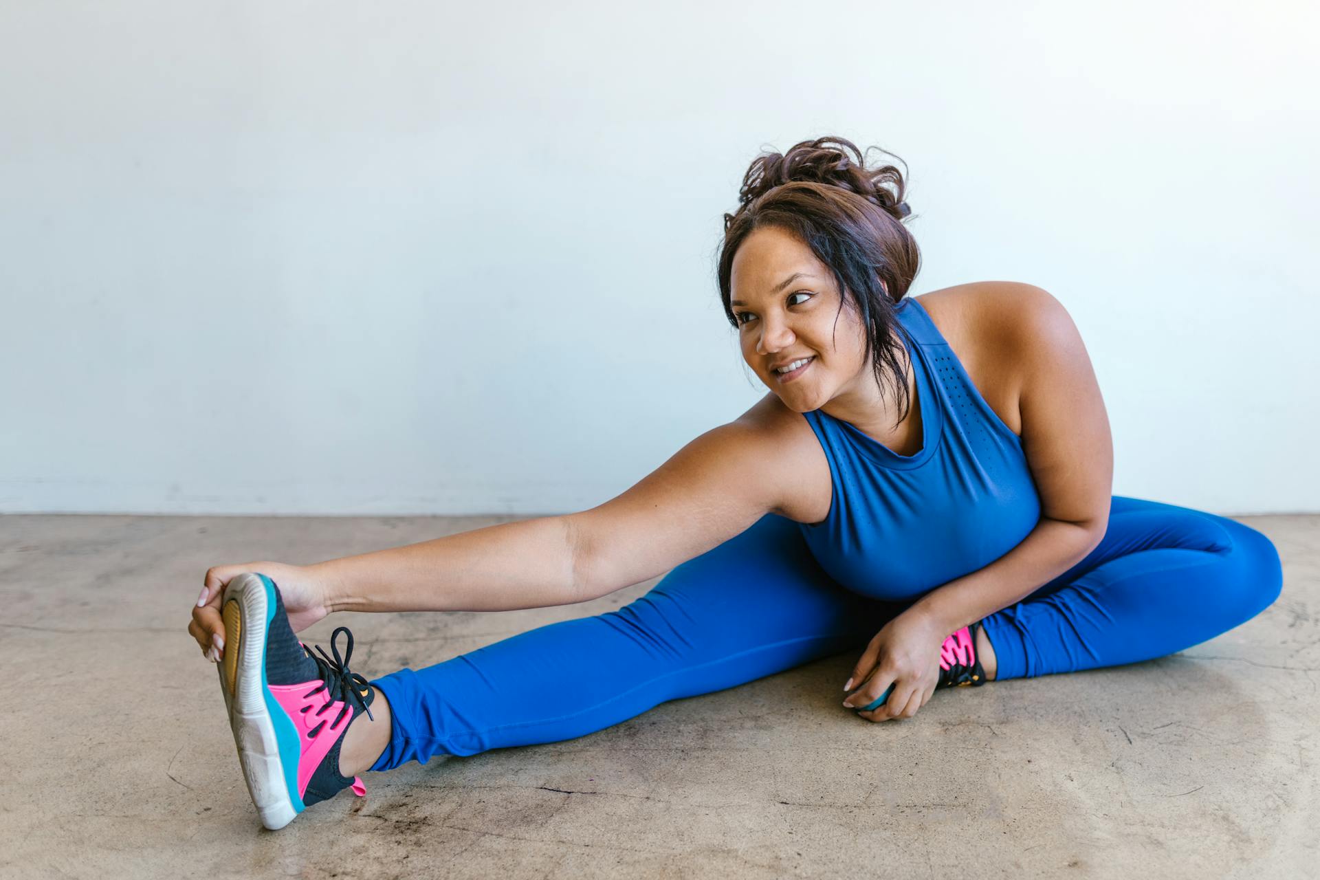 A plus-size woman in blue activewear stretching indoors, promoting body positivity and wellness.