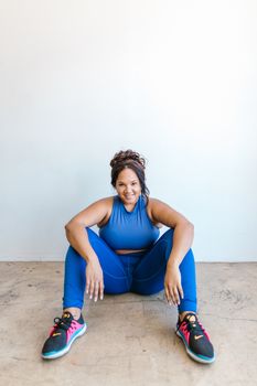 Confident plus-size woman sitting casually in blue activewear, smiling.