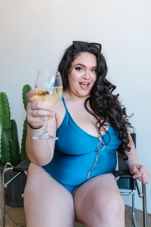 Free Plus-size woman sitting comfortably in blue swimwear, embracing self-love and body positivity while holding a wine glass. Stock Photo