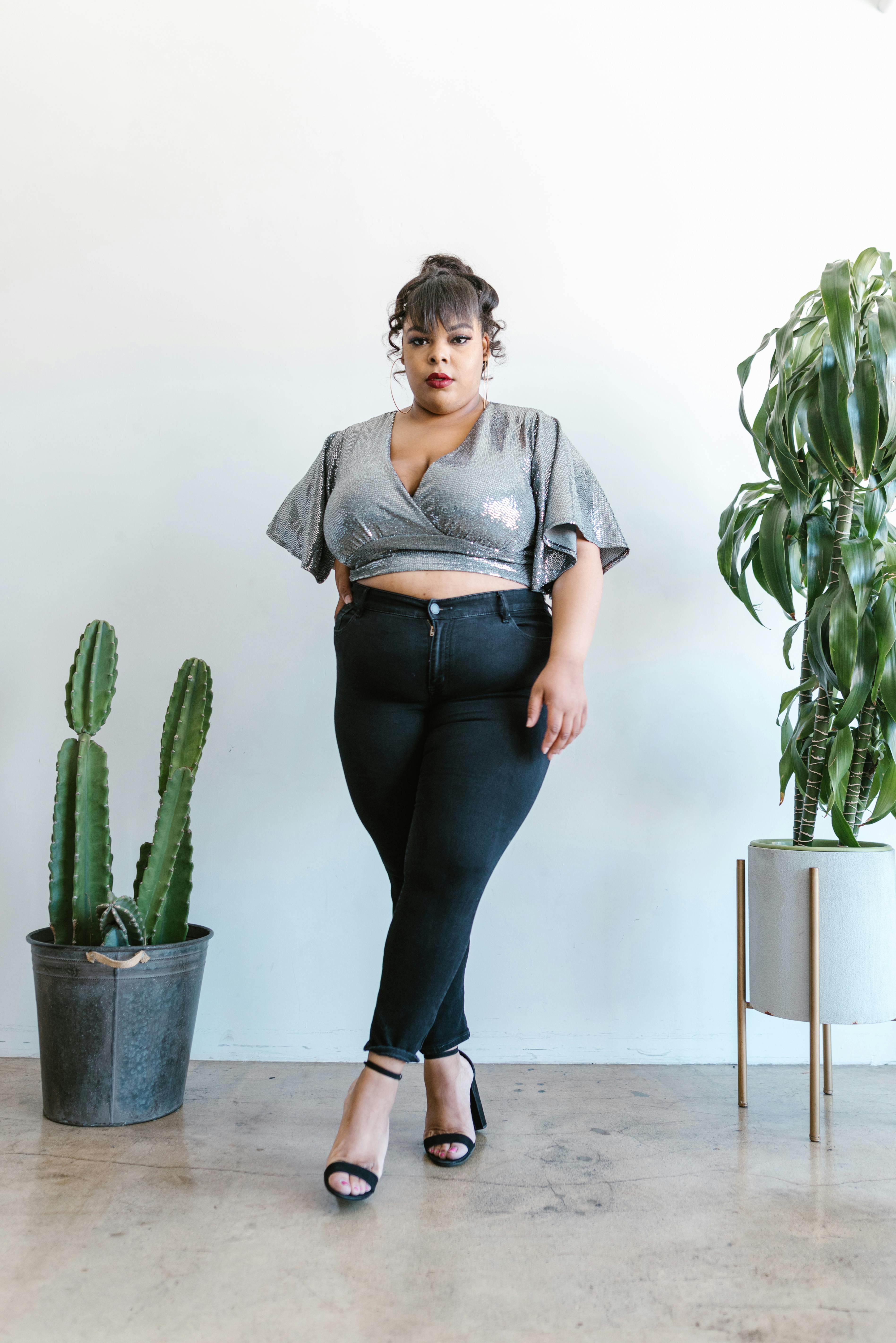 a woman in gray blouse and jeans is standing beside cactus plant