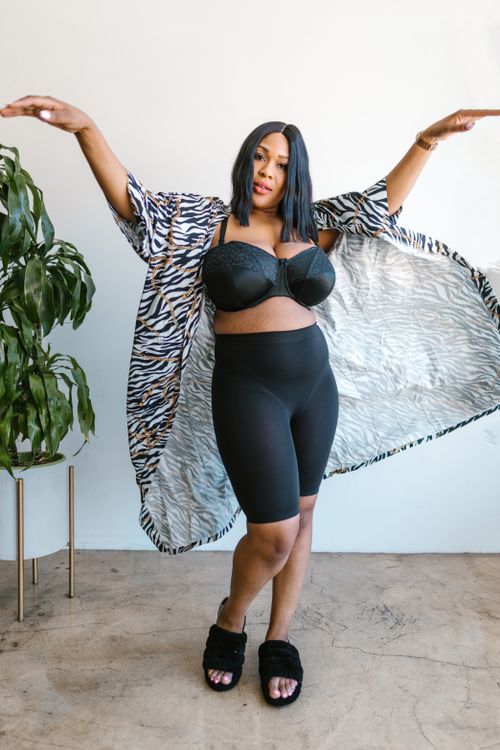 Free Plus-size woman posing confidently in a zebra-print robe and black lingerie indoors. Stock Photo