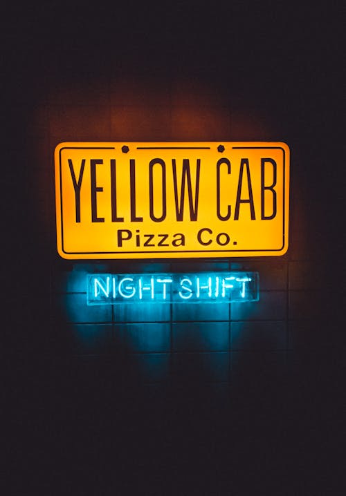 Colorful signboard of modern public pizzeria with inscription and neon lights hanging on wall during night shift on dark street