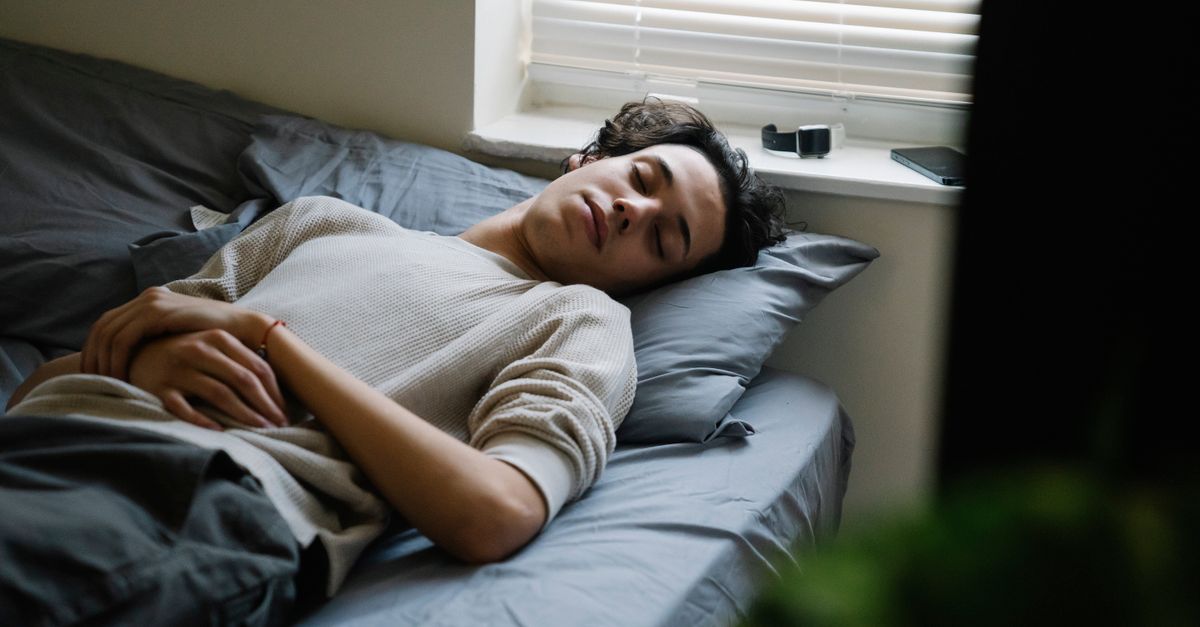 A man calmly sleeps on a bed in a cozy bedroom with soft lighting.