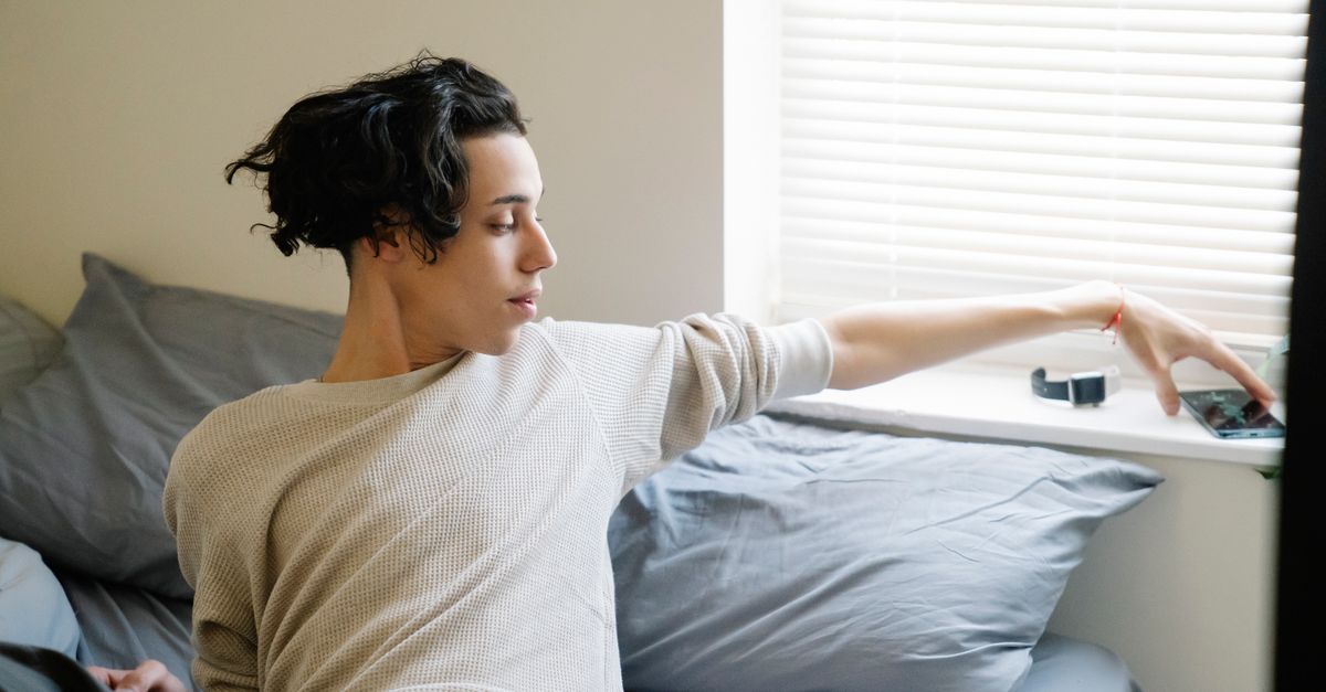 person checking phone in bed with morning sunlight