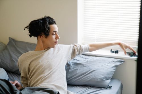 Free Young ethnic male adolescent taking mobile phone from windowsill after awakening in morning in bedroom Stock Photo