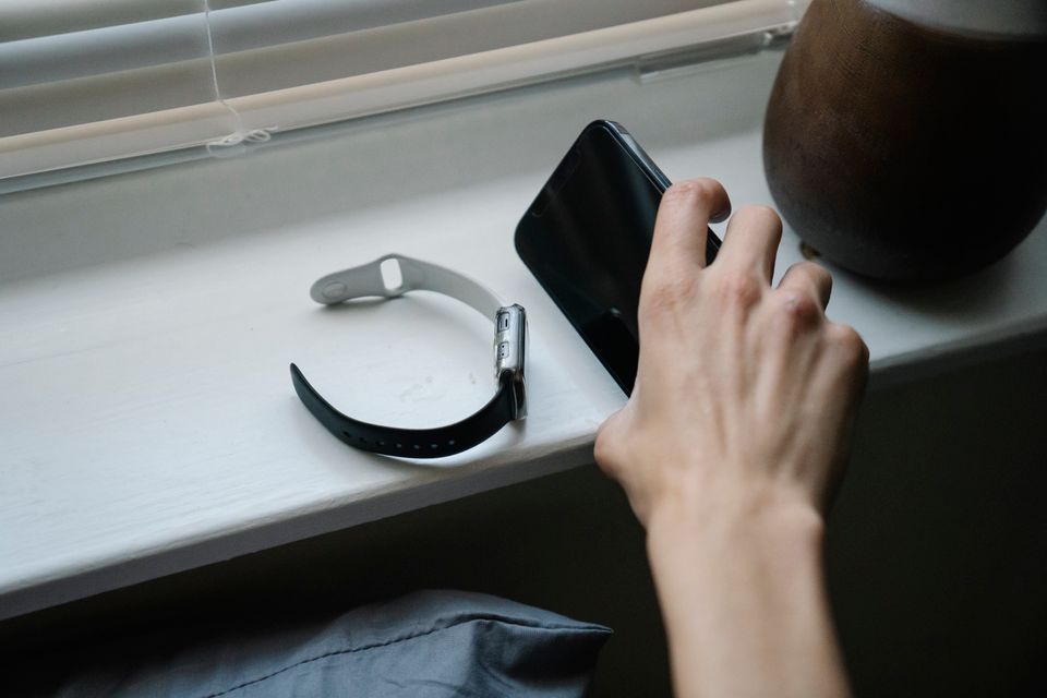 寝室でスマートフォンの隣にスマートウォッチを置く場面のイメージ。Appleのヘルスケアアプリ画面ではない