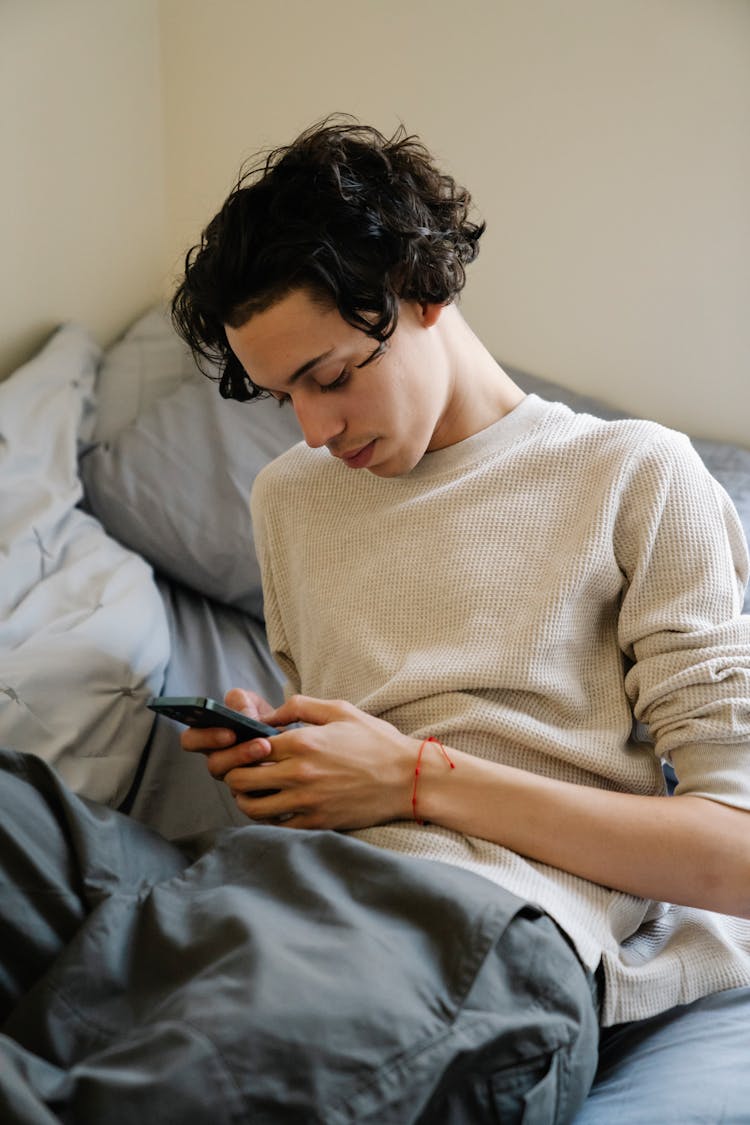 Young Hispanic Man Using Smartphone On Bed