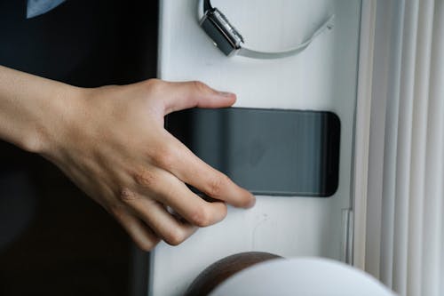Free Top view of anonymous person taking cellphone with black screen from windowsill near wristwatch at home Stock Photo