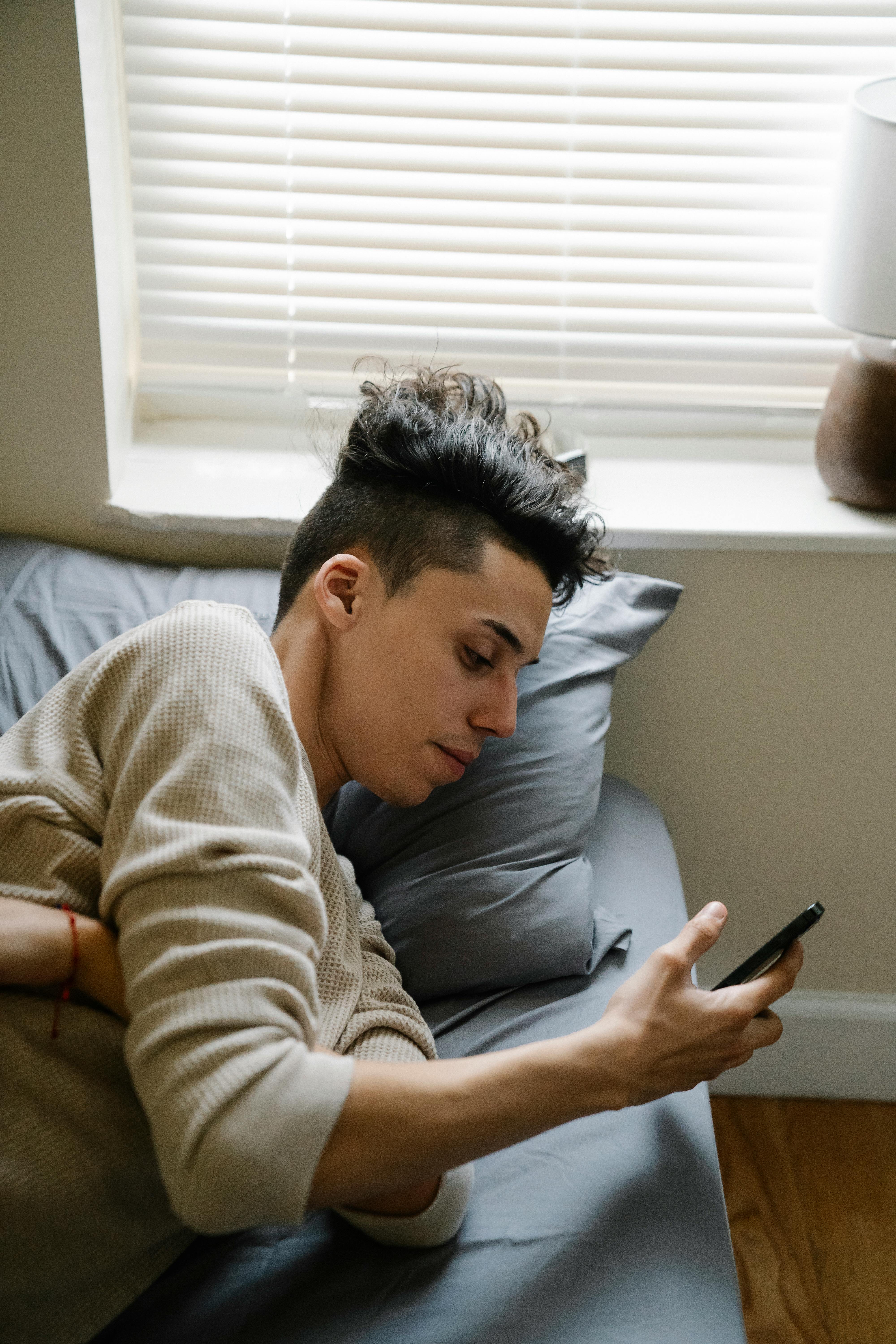 young hispanic male with smartphone lying on bed