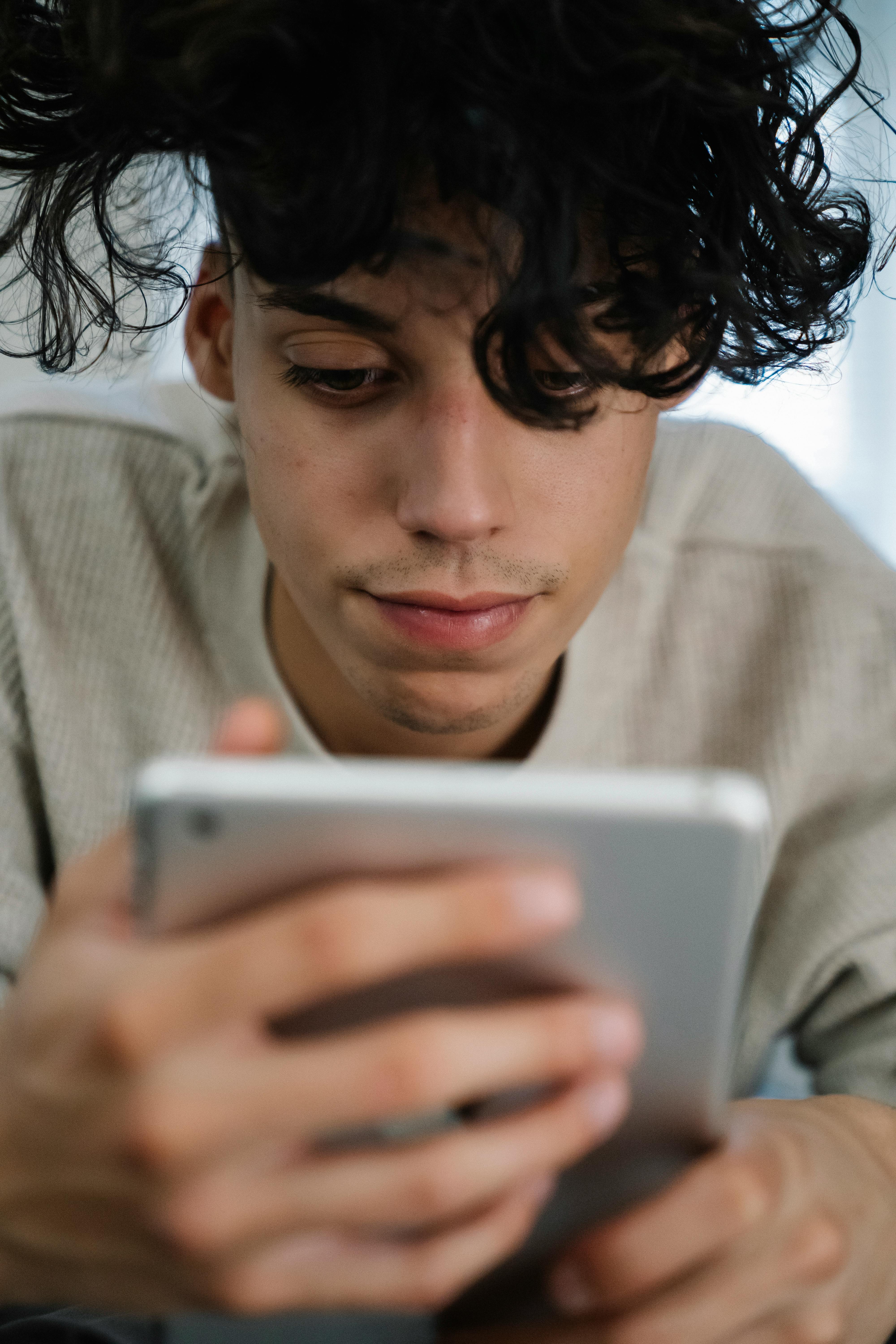 Young man with curly hair using a tablet indoors, portraying a relaxed and casual lifestyle.