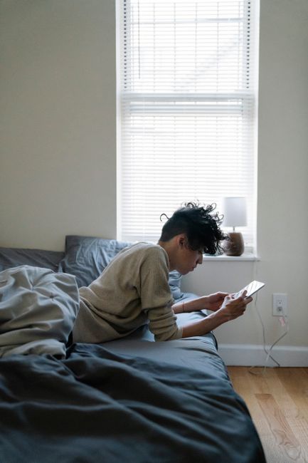 Young man lying on bed using smartphone in a modern indoor setting.