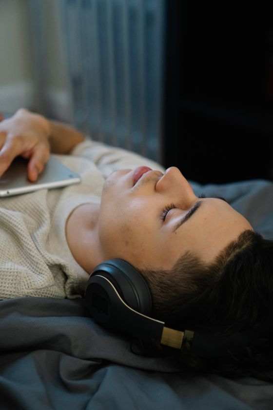 A man lying down at home with headphones on and his eyes closed. Photo by Eren Li on Pexels.