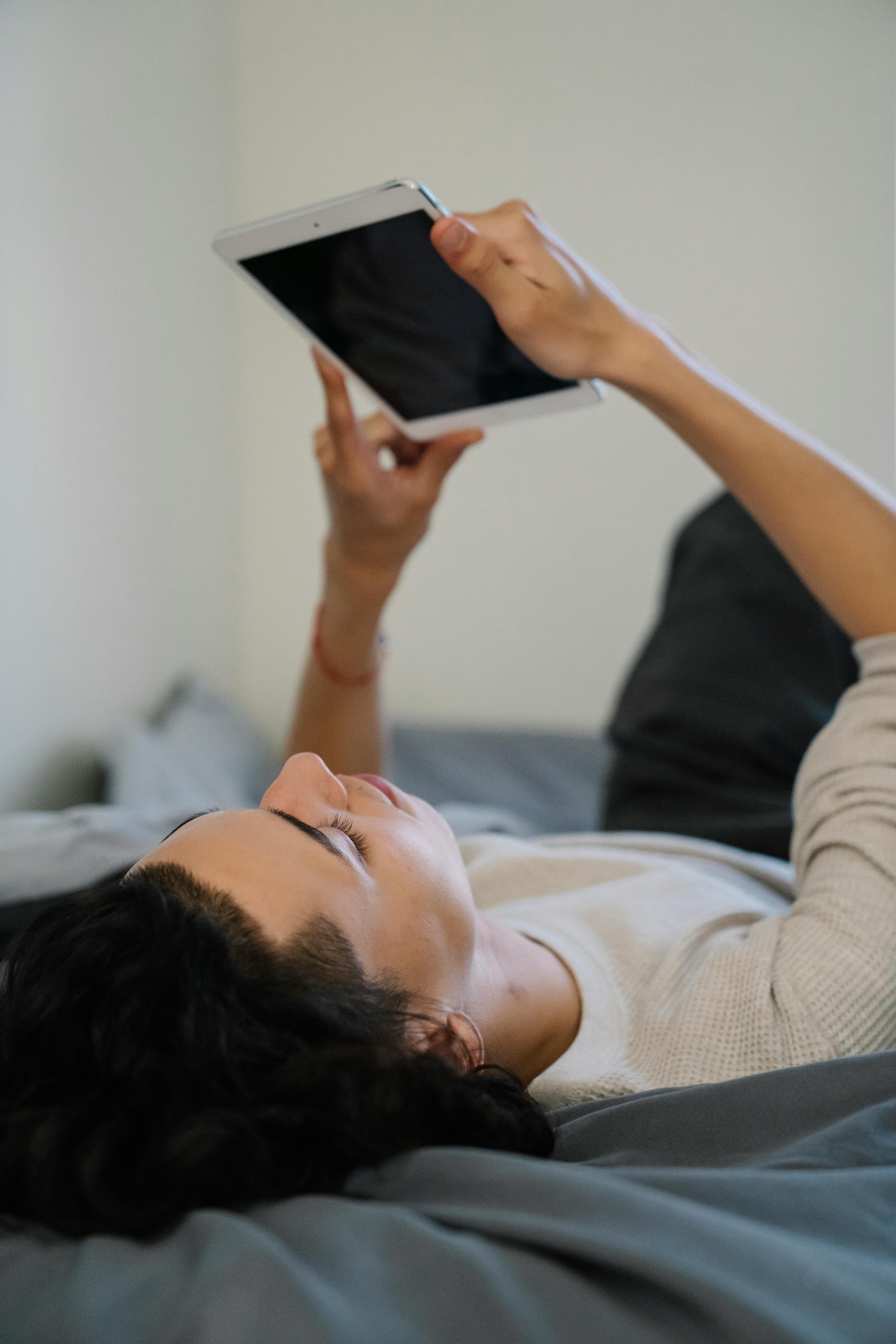young male lying on bed and browsing tablet
