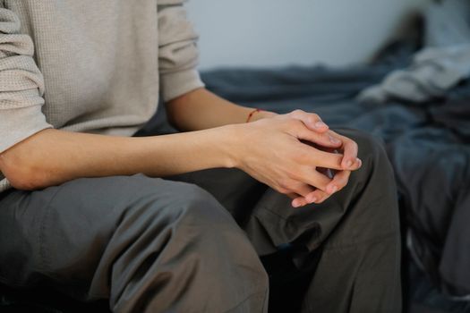 Unrecognizable young male in casual clothes sitting on bed and resting on weekend day at home