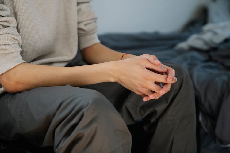 Crop Young Man Sitting On Bed At Home