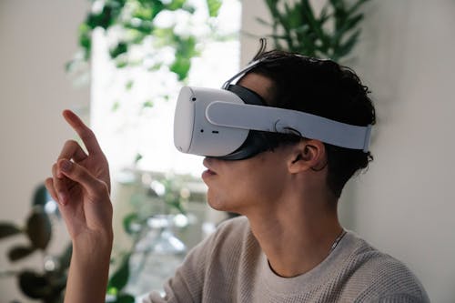 Free Side view of concentrated young guy in casual clothes experiencing virtual reality in modern headset at home Stock Photo