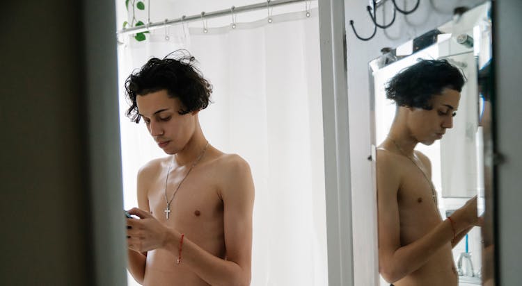 Focused Young Ethnic Male With Naked Torso Messaging On Smartphone In Bathroom