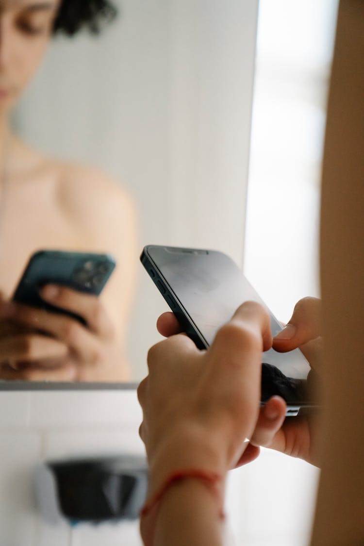 Person Using Smartphone Near Mirror In Light Room