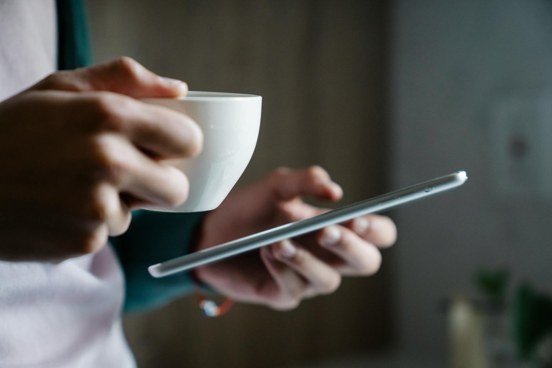 A close-up shot of a person holding a cup of coffee and a smartphone