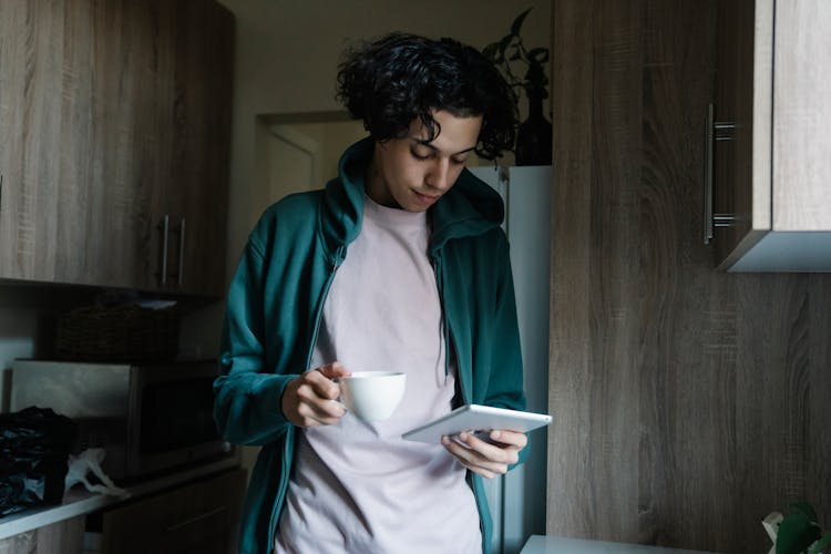 A Man Holding A Cup Of Coffee And A Tablet