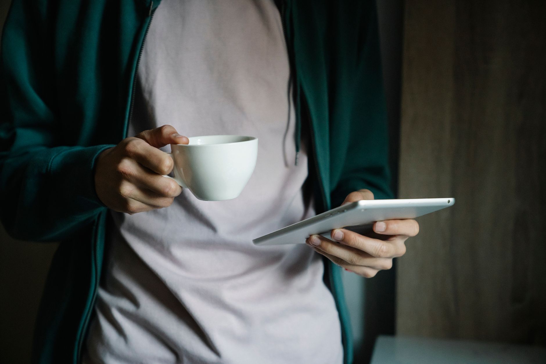 Close-up of hands holding a tablet and cup, suggesting a relaxed technology browse.