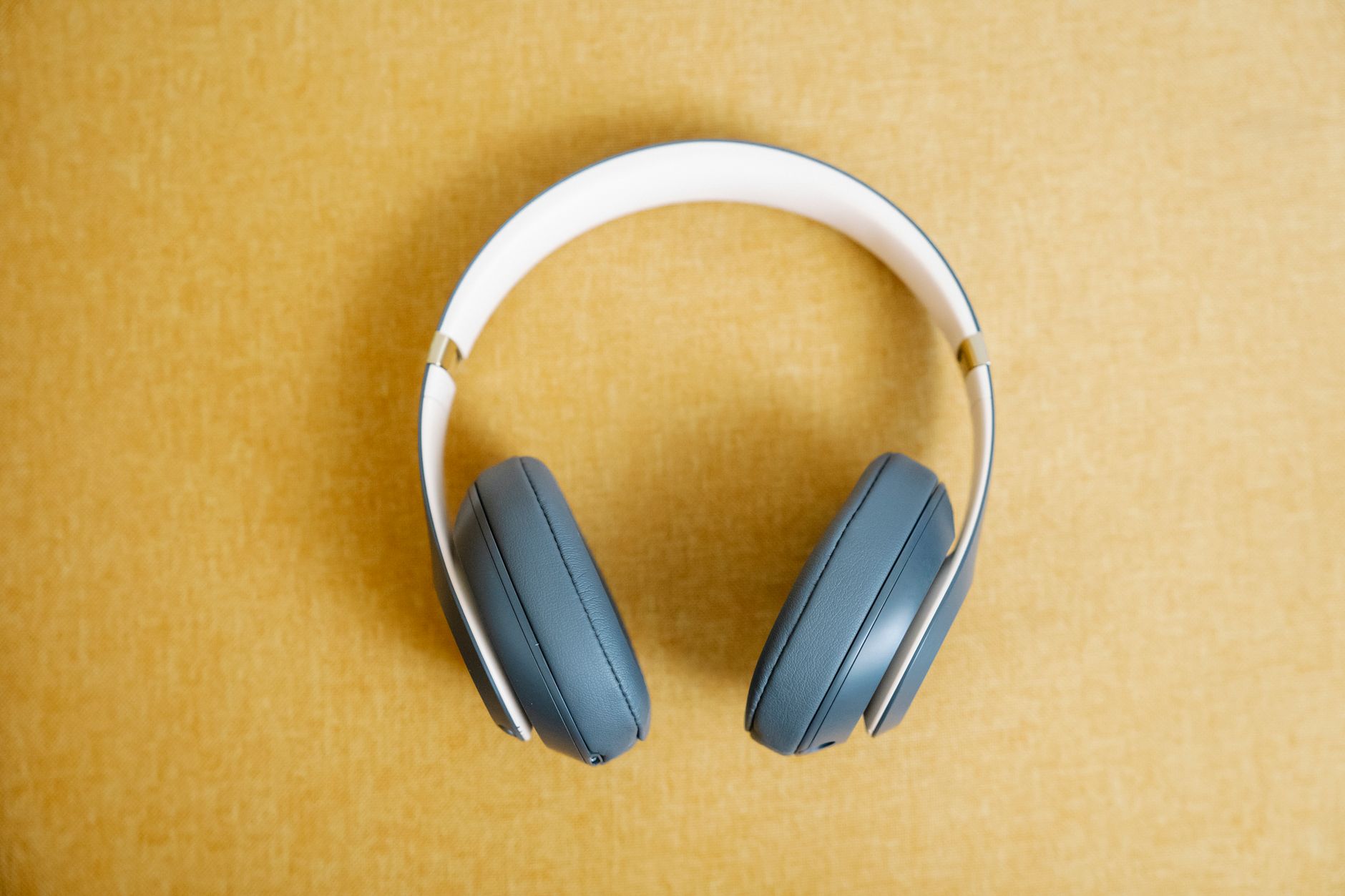 Blue wireless headphones on a yellow background, showcasing modern design and style.