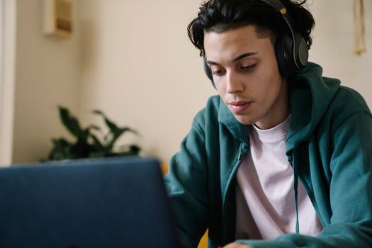 Crop serious male student in casual wear and headphones preparing for lessons on laptop and looking down