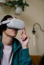Low angle of male pointing up while sitting on sofa in modern VR goggles at home