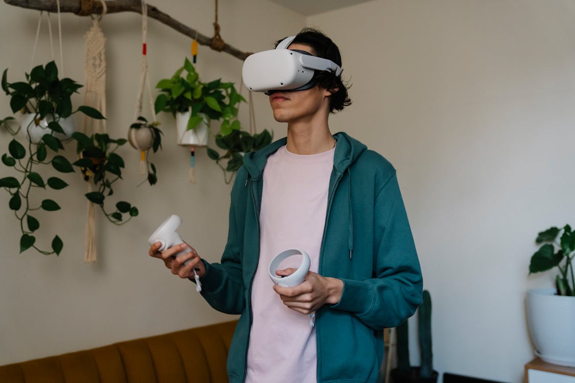 Man in virtual reality headset with controllers playing video game against potted plants in house room