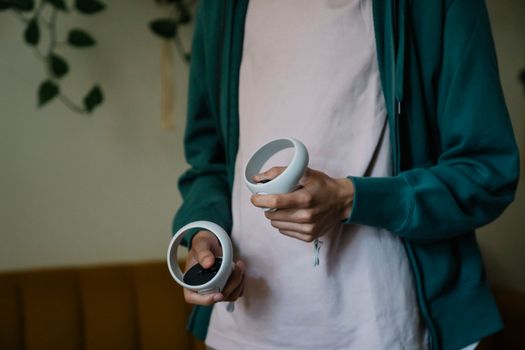 Crop anonymous male with virtual reality controllers playing video game in house room on blurred background