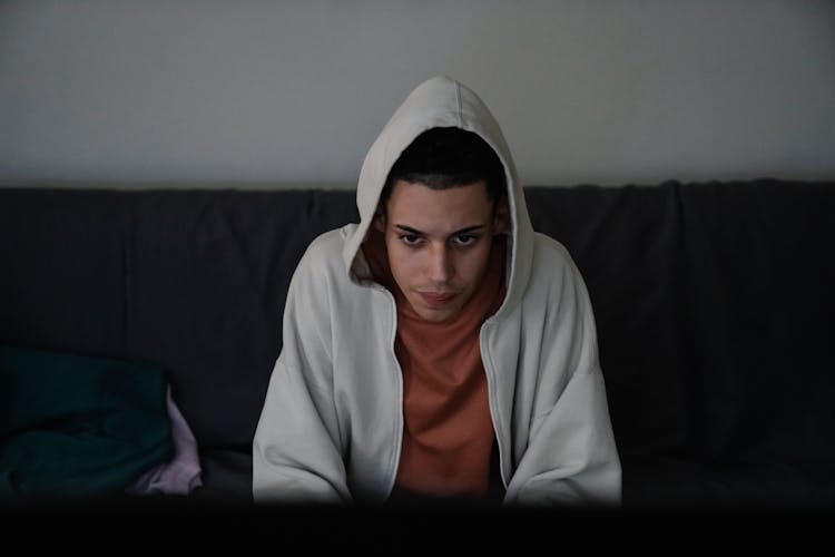 Focused Ethnic Man In Hoodie On Couch In House