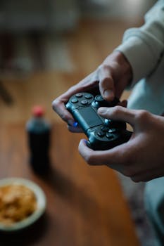 Crop unrecognizable man with console controller pressing buttons while playing video game at home in daylight
