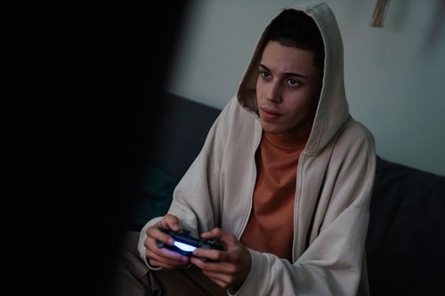 Free Addictive young ethnic male gamer in hoodie with console controller playing video game while looking forward at home Stock Photo