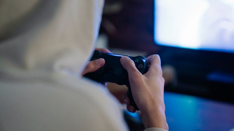 Back view of crop anonymous man with console controller playing video game against screen at home