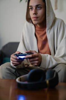 Crop addictive young ethnic male gamer with console controller playing video game while looking forward on couch at home