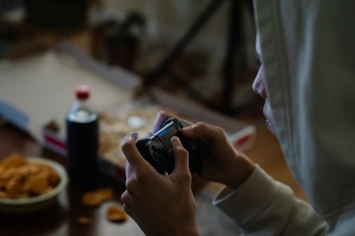 Free Side view of crop young man in hood with joystick playing video game while having spare time at home Stock Photo
