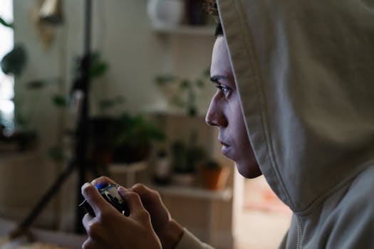 Side view of crop focused ethnic male gamer with console controller playing video game while looking forward in house